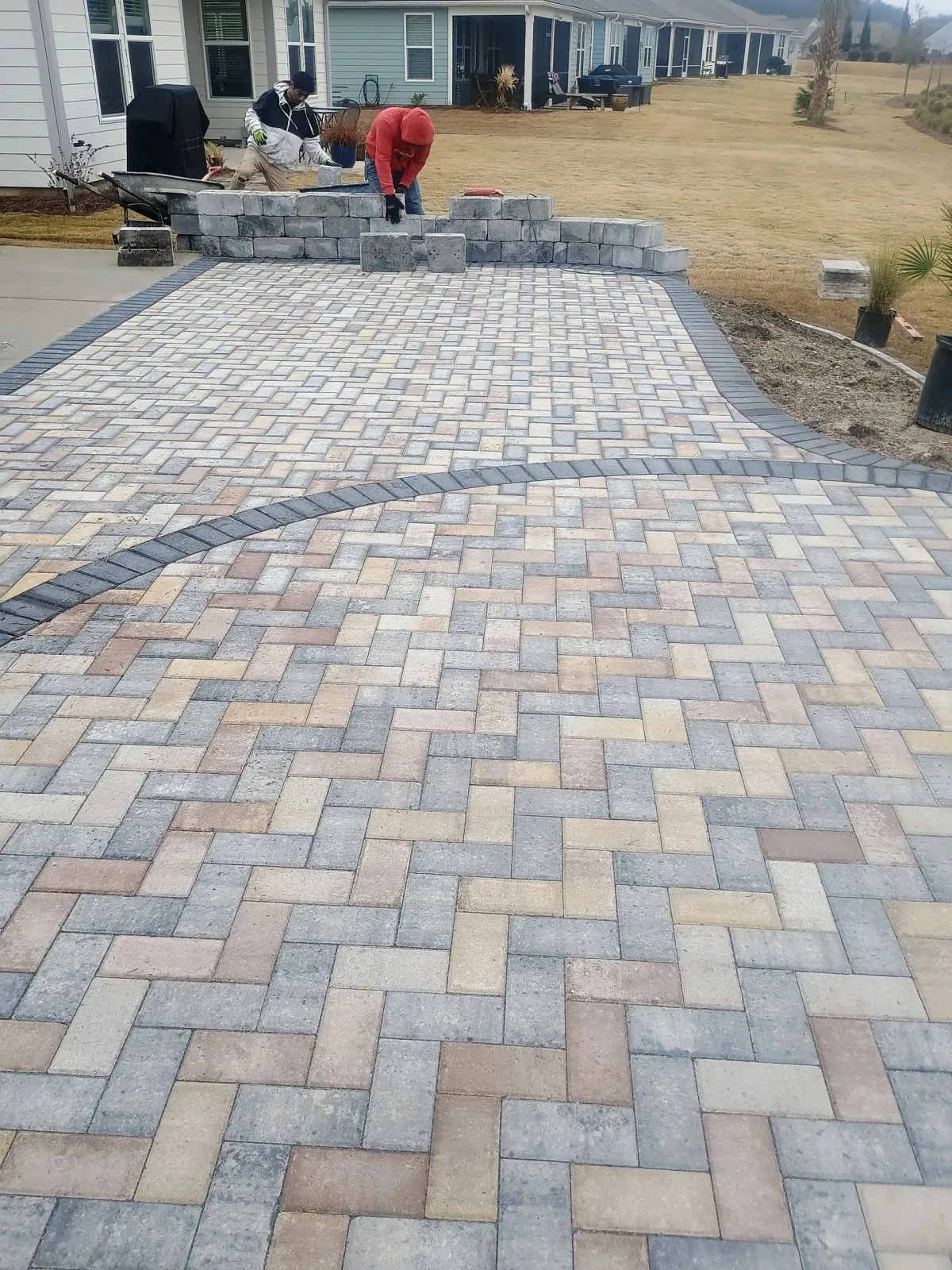 Curved red brick patio with a circular brick fire pit and pale stones in the center