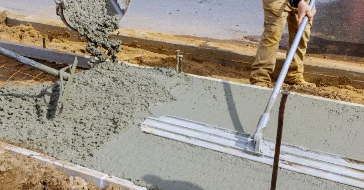 Fresh concrete driveway leading to a gray house with fenced sides and dirt along the edges